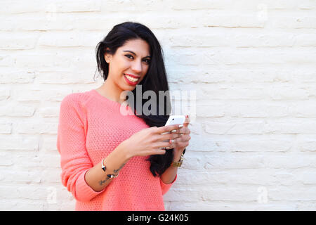 Belle jeune femme latine des SMS sur son téléphone. Femme à l'aide d'un cellulaire portant des vêtements décontractés. Banque D'Images