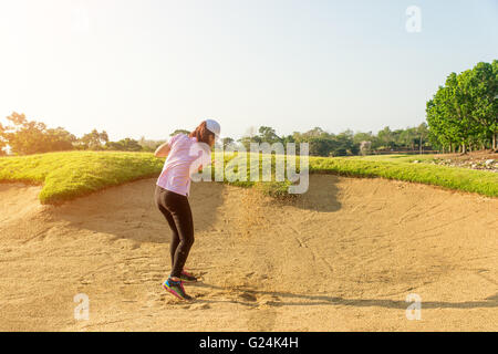 Asian woman golfer hitting balle de golf hors d'une trappe de sable Banque D'Images