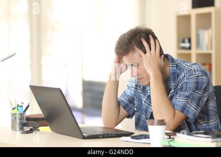 Inquiet et triste homme étudiant regarder les résultats de l'examen à la ligne dans un ordinateur portable dans un bureau à la maison prix Banque D'Images