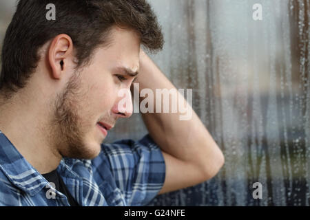 Vue latérale d'un homme triste à la fenêtre grâce à des larmes dans un jour de pluie Banque D'Images