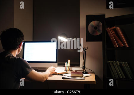 Vue arrière du jeune homme asiatique concentrared travail avec ordinateur écran vide in dark room Banque D'Images