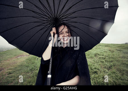 Portrait of smiling Woman holding umbrella in wind Banque D'Images