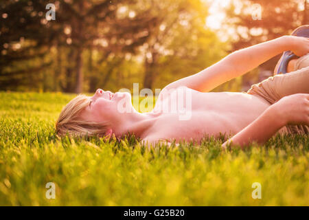 Garçon couché sur l'herbe en riant jardin Banque D'Images