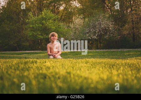 Garçon assis dans un jardin à l'herbe Banque D'Images
