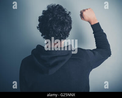 Vue arrière Vue d'un jeune homme dans un haut à capuchon élever son poing en l'air Banque D'Images