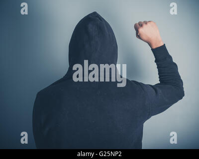 Vue arrière Vue d'un jeune homme dans un haut à capuchon élever son poing en l'air Banque D'Images