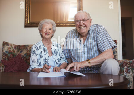 Portrait of a smiling couple de retraités à la recherche de plus de documents. Young man and woman sitting on sofa at home et la vieillesse Banque D'Images