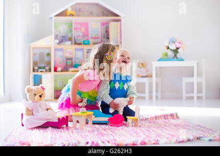 Les enfants jouent avec maison de poupée peluche et jouets. Les enfants sont assis sur un tapis rose dans une salle de jeux à la maison ou au jardin. Banque D'Images