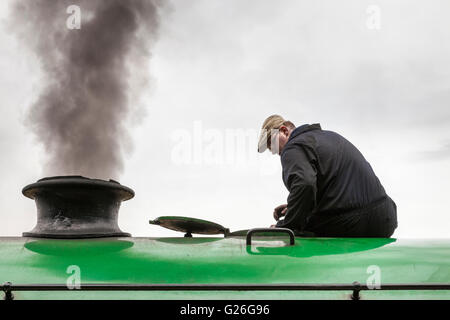 Conducteur de locomotive ou fireman assis sur une chaudière à vapeur avec de la fumée sortant de la cheminée, Lancashire, England, UK Banque D'Images