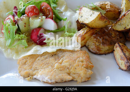 Escalope de poulet un plat composé de pommes de terre au four, salade et sur plaque blanche. Bol à salade couché sur faits de fromage mozzarella. Banque D'Images