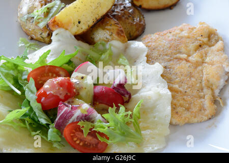 Escalope de poulet un plat composé de pommes de terre au four, salade et sur plaque blanche. Bol à salade couché sur faits de fromage mozzarella. Banque D'Images