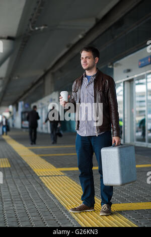 Portrait de jeunes happy smiling handsome man voyageur en 20s de quitter le salon de l'aéroport arrivées terminal après avoir récupéré ses bagages avec une tasse de café frais Banque D'Images