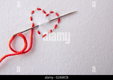 Coeur rouge brodé sur un drap blanc close up. Concept passion pour la couture et broderie. Composition horizontale.vue d'en haut Banque D'Images