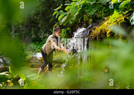 Femme dans la nature, avec des feuilles vertes, laver ses mains à la cascade Banque D'Images