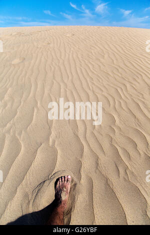 Les jambes d'un homme marchant et laissant imprimer des pieds sur le sable Banque D'Images