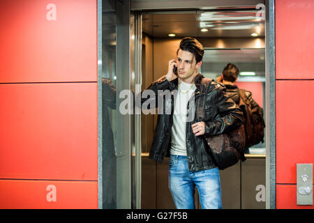 Beau jeune homme appuyé contre miroir à l'intérieur d'un ascenseur ou d'ascenseur, d'appeler quelqu'un on cell phone Banque D'Images