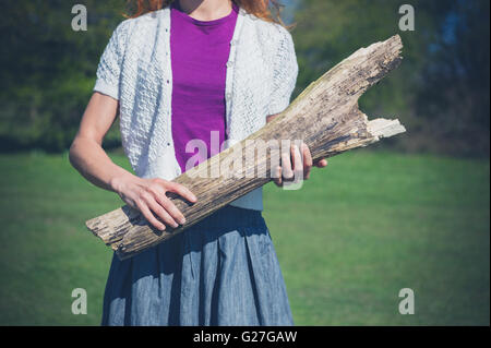Une jeune femme se tient debout sur l'herbe dans une clairière d'une forêt et est maintenant un grand log Banque D'Images