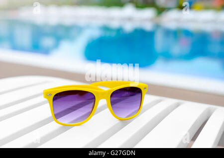 Lunettes de soleil jaune sur une chaise longue près de la piscine. Close-up. Banque D'Images