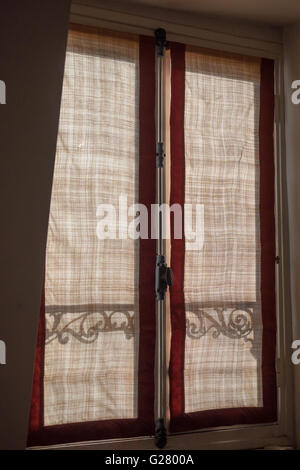 Le soleil jette une ombre de motif silhouette rail balcon contre sur un filet de jute rideau sur une charpente en bois fenêtre parisienne Paris France Banque D'Images