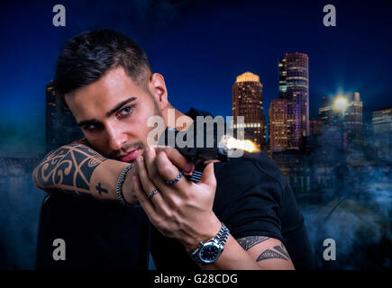 Portrait de beau jeune homme tatoué avec des coups de fusil contre quelqu'un la nuit dans la ville Banque D'Images