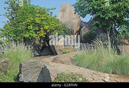 Sentier sinueux pavée de dalles en pierre de granit rugueux, allant jusqu'à travers un terrain vallonné avec d'énormes rochers et arbustes. Banque D'Images