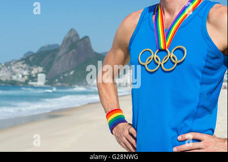 RIO DE JANEIRO - Mars 10, 2016 : l'athlète Gay se dresse sur la plage d'Ipanema portant des anneaux olympiques médaille d'or avec ruban arc-en-ciel. Banque D'Images