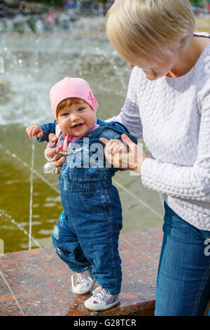 Petite fille fait le premier pas avec sa mère près de la fontaine Banque D'Images