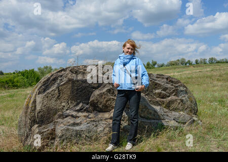 De la femme en bleu veste est posant près de big split off boulder sur champ sauvage à la banque du Dniepr. Banque D'Images