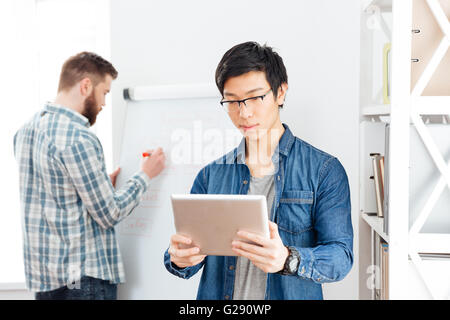 Deux jeunes hommes d'concentré travailler avec tablet et un tableau-in office Banque D'Images