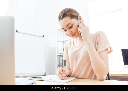 Smiling young woman talking on mobile phone in office Banque D'Images
