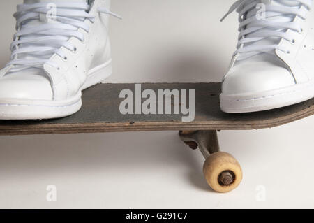 L'homme à nettoyer les formateurs blanc faisant des tours sur un vieux skateboard Banque D'Images