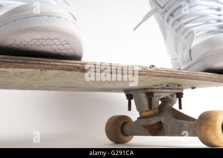 L'homme à nettoyer les formateurs blanc faisant des tours sur un vieux skateboard Banque D'Images