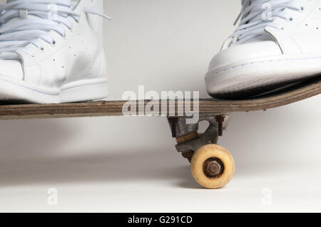 L'homme à nettoyer les formateurs blanc faisant des tours sur un vieux skateboard Banque D'Images