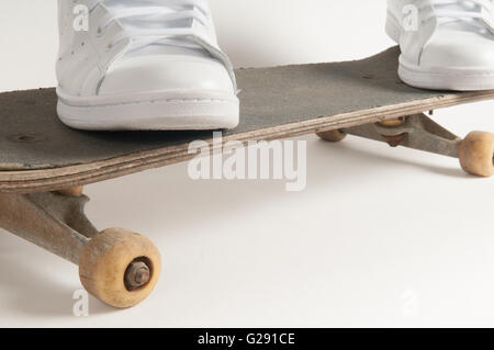 L'homme à nettoyer les formateurs blanc faisant des tours sur un vieux skateboard Banque D'Images