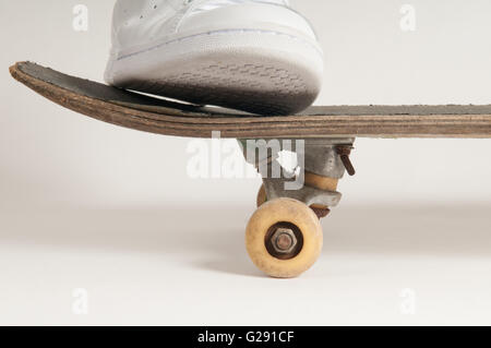 L'homme à nettoyer les formateurs blanc faisant des tours sur un vieux skateboard Banque D'Images