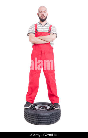 Mechanic standing confiant avec les bras croisés sur le haut de la roue de voiture isolated on white Banque D'Images