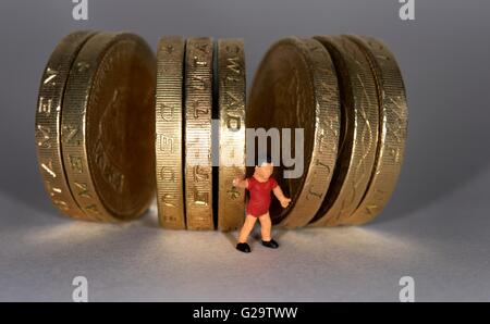 Un petit garçon debout figurine miniature entre British une livre de monnaie. Banque D'Images