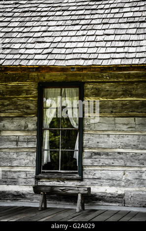 Une fenêtre avec des rideaux tirés sur une cabane rustique de charme avec véranda et siège dans un style 19ème siècle nostalgique Banque D'Images