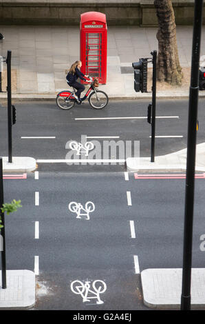 Une vue aérienne d'un cycliste à une voie cyclable passant une boîte de téléphone rouge avec trois signes du cycle sur le remblai à Londres Banque D'Images