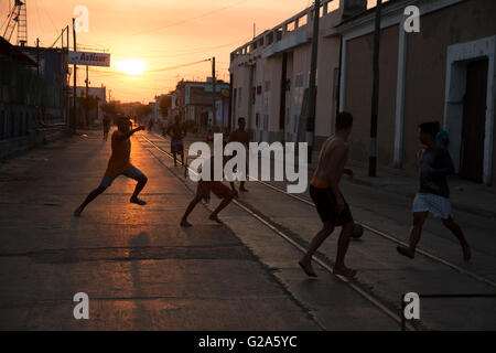 Silhouettes d'adolescents cubains jouant au football dans la rue que le soleil se couche derrière eux à Cienfuegos Cuba Banque D'Images