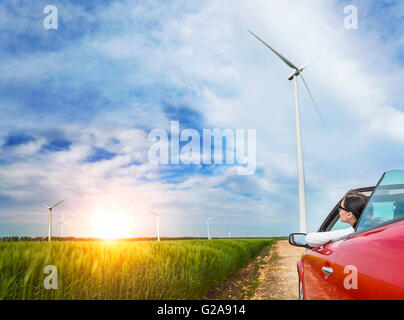 Girl in red cabriolet dans un champ avec des éoliennes au coucher du soleil. Banque D'Images