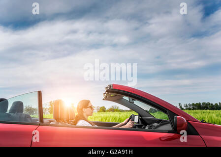 Girl in red cabriolet dans un champ avec des éoliennes au coucher du soleil. Banque D'Images