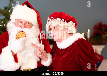 Mme Claus pointant sur Santa eating gingerbread cookie Banque D'Images