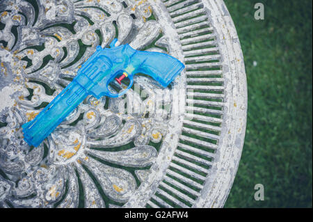 Un pistolet à eau bleu allongé sur une vieille table dans un jardin Banque D'Images