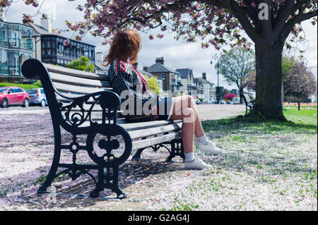 Une jeune femme est assise sur un banc de parc avec fleur de cerisier sur le terrain Banque D'Images