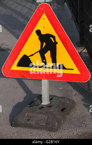 Triangle de signalisation rouge et jaune se dresse sur le bord de la route. L'homme au travail, en construction routière Banque D'Images