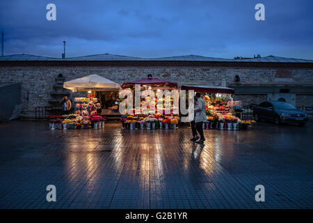 Un jeune couple à pied passé étals de fleurs sur un soir de pluie sur la place Taksim, à Istanbul. Banque D'Images