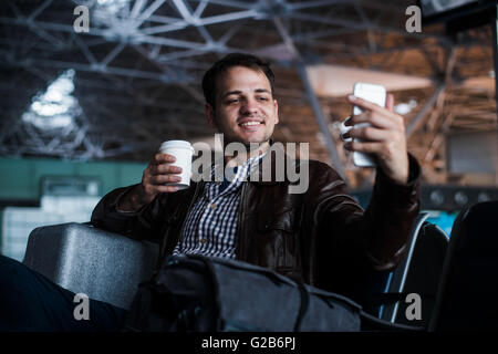 Portrait d'un jeune homme de rire et de prendre le café avec selfies à l'aéroport en attendant son vol Banque D'Images