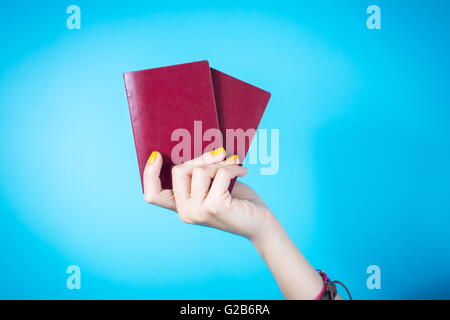 Womans hand holding a deux passeport rouge contre bleu fond Banque D'Images