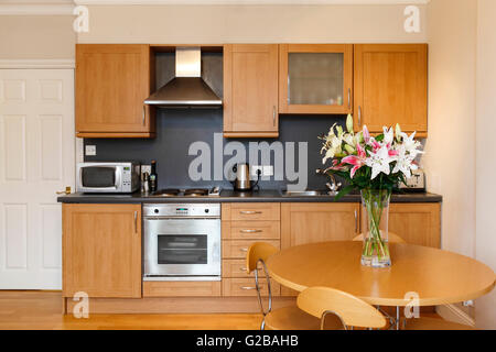 Maison Molyneux, Marble Arch. Petite cuisine moderne avec table à manger. Vase en verre avec des fleurs sur la table. Des armoires en bois et en acier inoxydable. Banque D'Images